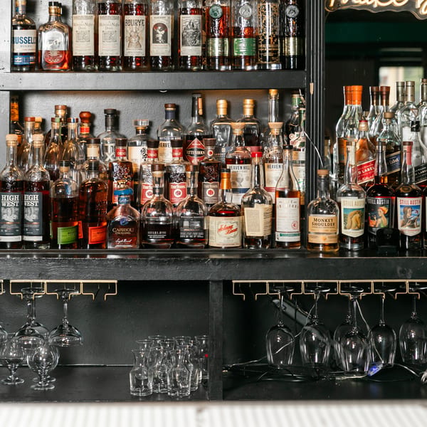 A well-stocked bar shelf displays numerous bottles of liquor, with hanging glasses below.