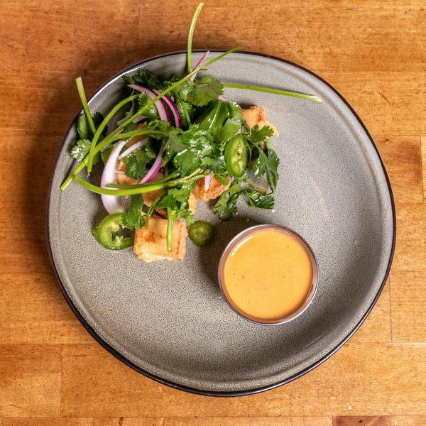 Crispy fried tofu with fresh cilantro, red onion, jalapeño, and a side of orange dipping sauce.