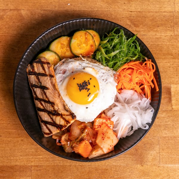 A colorful bibimbap bowl with grilled salmon, fried egg, kimchi, and various vegetables.