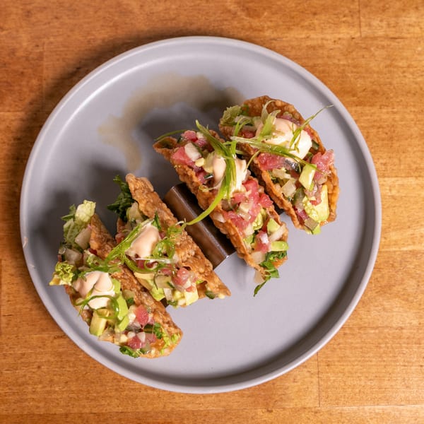 Four tuna poke tacos with avocado, sauce, and scallions on a gray plate.