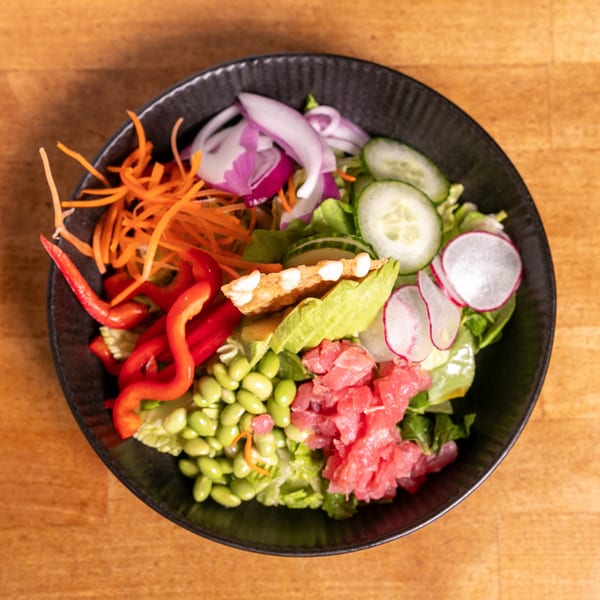 Overhead view of a colorful salad with tuna, avocado, edamame, and vegetables in a black bowl.