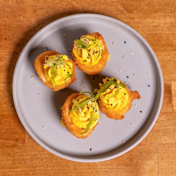 Four crispy deviled eggs topped with yellow filling, green onions, and sesame seeds on a gray plate.